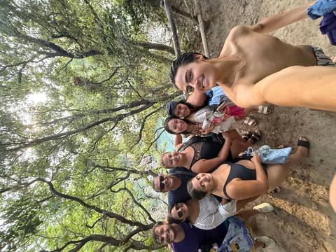 Group of people posing in a wooded area with a view of water.