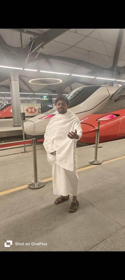 Person in white traditional attire at a train station with modern trains.