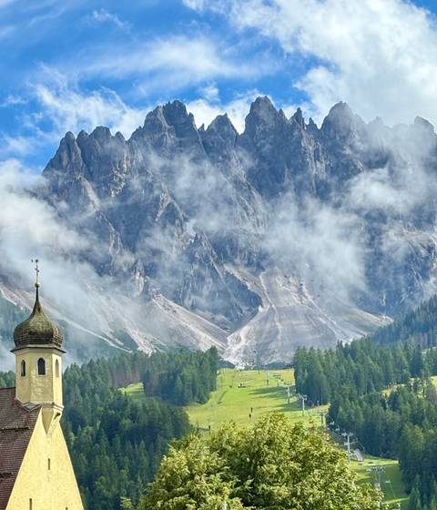       A scenic view of a picturesque mountain landscape partially covered in clouds with a church tower.
  