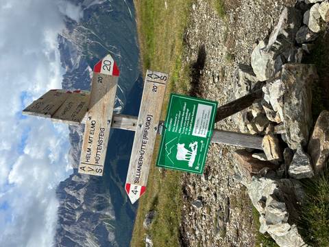       Directional signs on a hiking trail in the mountains under a cloudy sky.
  