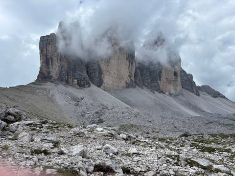       A stunning view of the Tre Cime di Lavaredo peaks with clouds hovering.
  