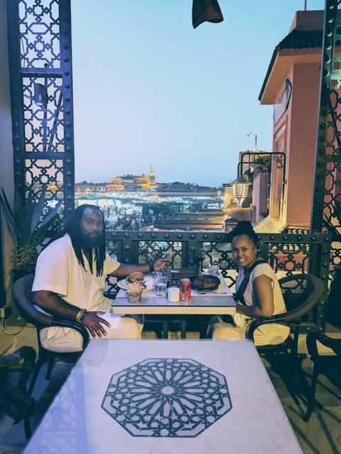 Couple dining on a balcony overlooking a city square.