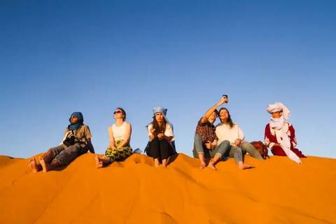 Group of people sitting on sand dunes in desert clothing.