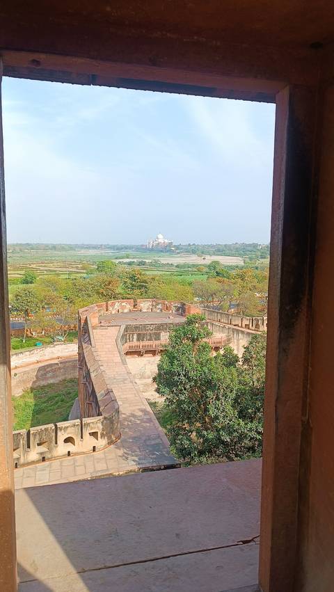 Landscape view of Taj Mahal from a distance, framed by trees.