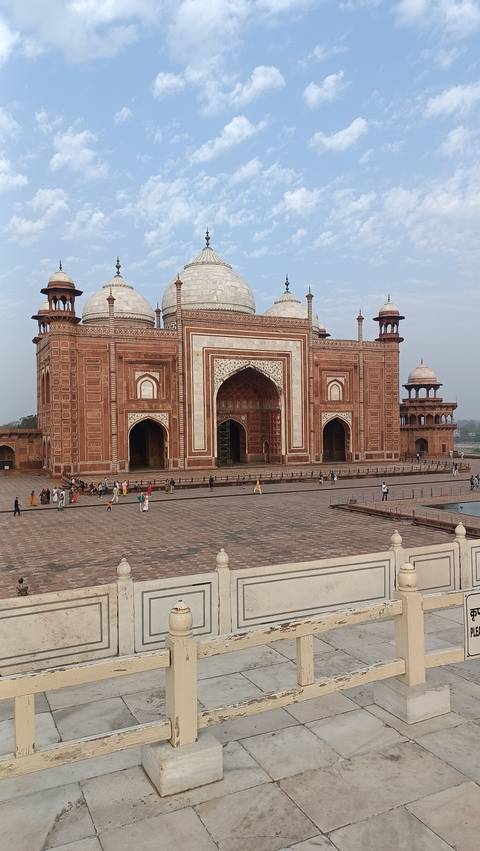 Red sandstone mosque courtyard with people walking.