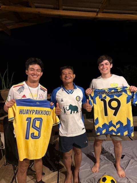 Three people holding sports jerseys posing with thumbs up.