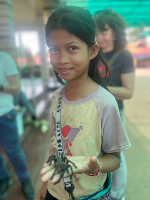       Smiling girl in a dusty shirt with people blurred in the background.
  