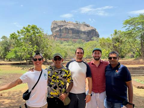 Group of people posing in front of Sigiriya Rock in a sunny environment.