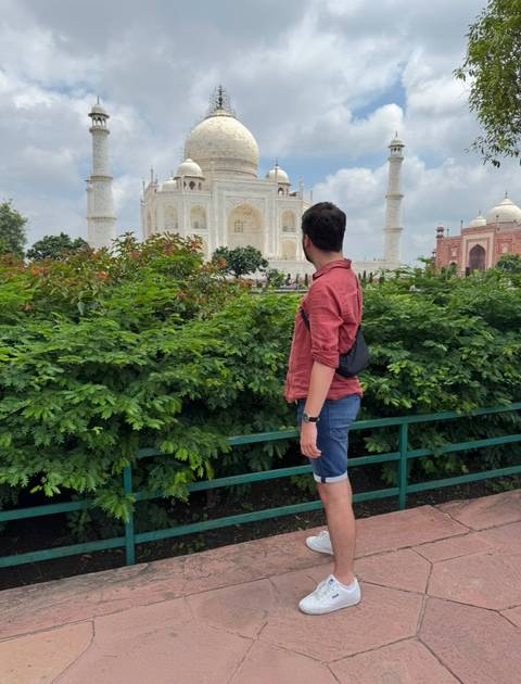 Person in front of the Taj Mahal, with greenery in the foreground.