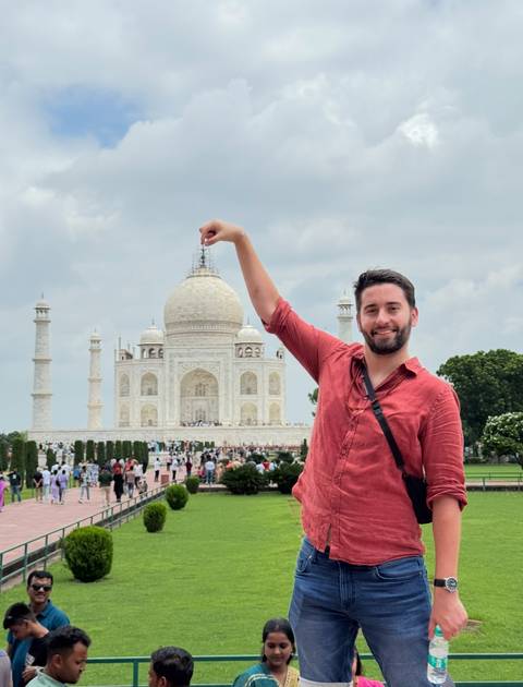 Person posing in front of the Taj Mahal, playfully interacting with the architecture.