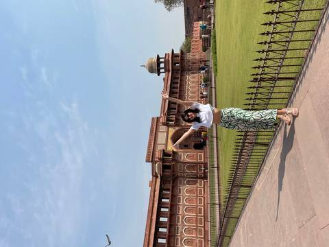 Person posing in front of Agra Fort, with arms raised.