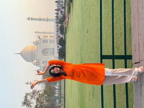 Person posing in front of the Taj Mahal during sunset.