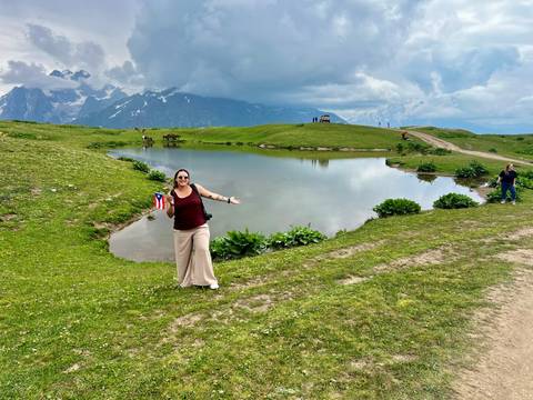 Person standing with arms out in front of a scenic alpine lake.