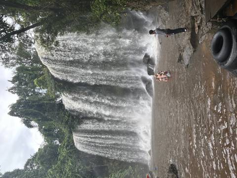       Tourists enjoying a natural waterfall in a lush forest setting.
  