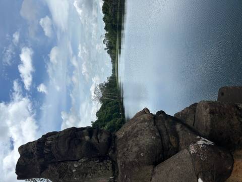 Statue on a bridge overlooking a tranquil river in a natural setting.
