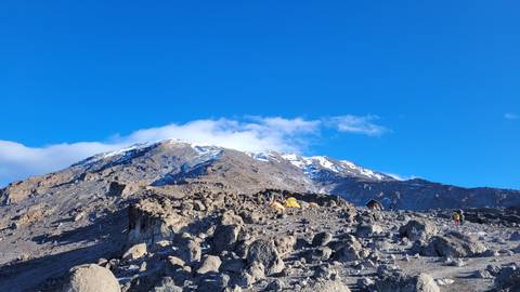       Rocky terrain leading to snow-capped mountains under clear blue sky.
  
