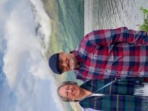       Two smiling people standing beside a lake with mountains.
  