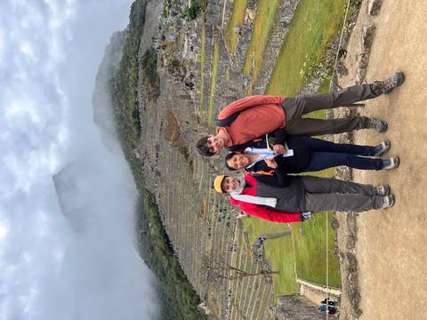 Three people posing with Machu Picchu in the background amidst a cloudy sky.
