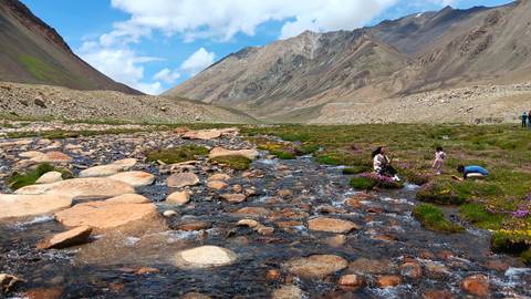 People by a clear stream with mountains in the background.