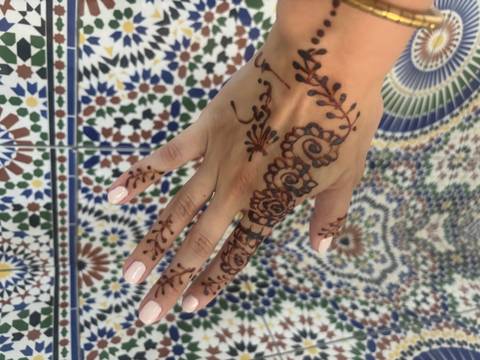       Hand with intricate henna design against a colorful tiled wall.
  
