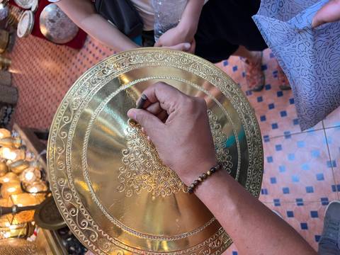 Close-up of hands crafting detailed patterns on a brass plate in a traditional setting.