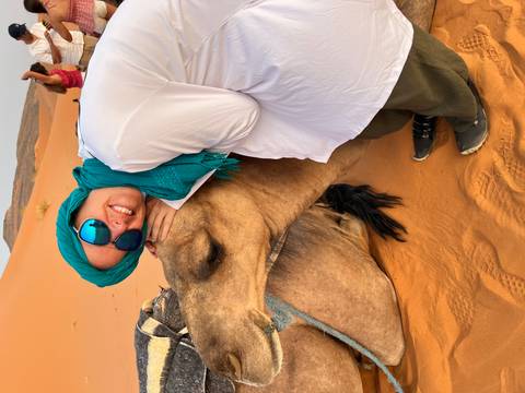       A woman embracing a camel while seated on the desert sands of Merzouga.
  