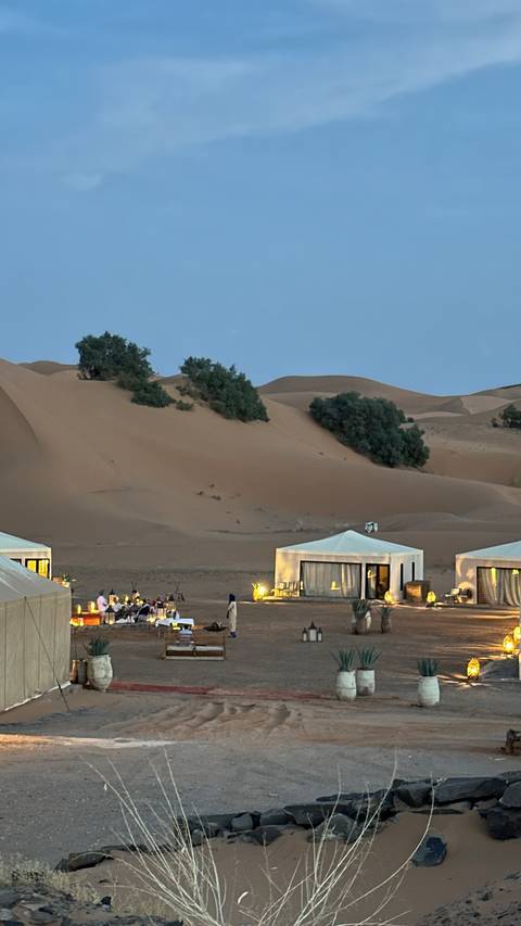 Luxury desert camp with tents set against tall sand dunes in Merzouga.