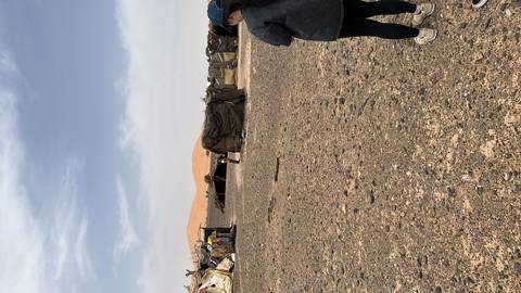 Desert nomad tents with people walking nearby on a rocky desert landscape.