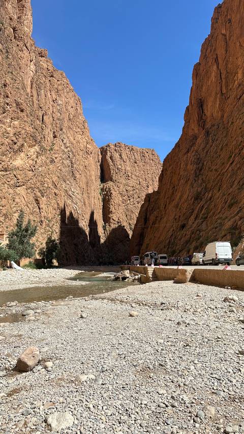 A narrow gorge with vehicles parked nearby and steep rocky walls.
