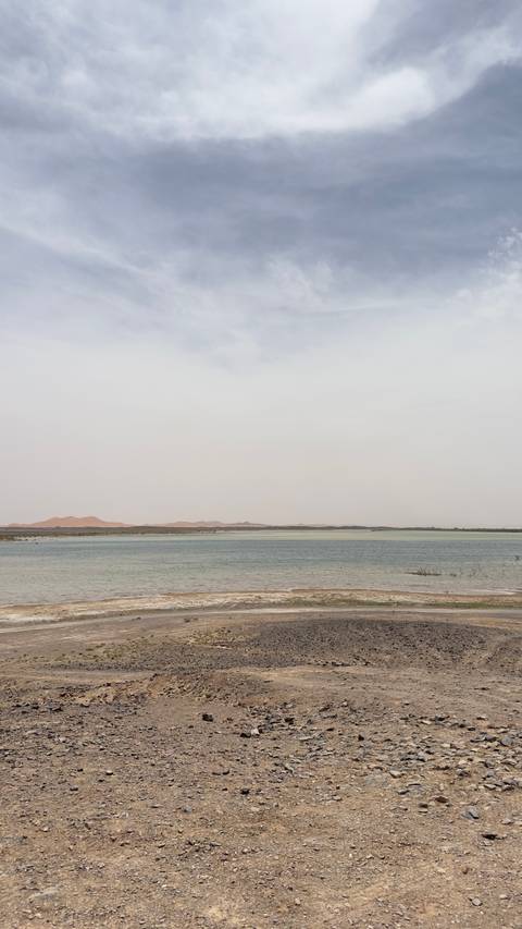 A vast lake in a desert landscape with distant mountains under a cloudy sky.