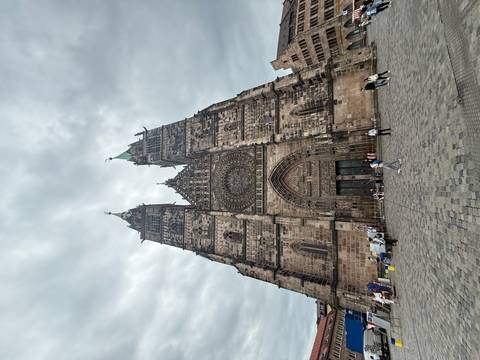       Large gothic-style church with two towers and a rose window, people in front.
  