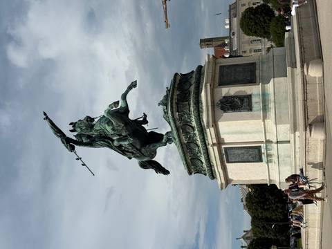       Statue of a man on horseback on a pedestal, with people around.
  
