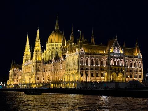       Lit up view of a grand building along the river at night.
  