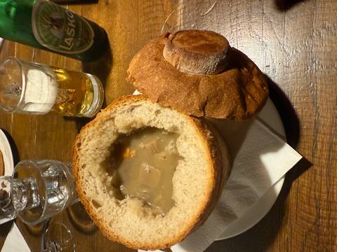       Bowl of soup in a bread bowl on a wooden table.
  
