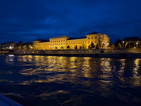       Nighttime riverside view with illuminated building reflected in the water.
  