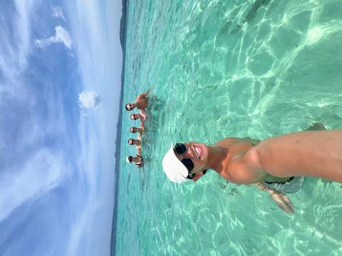       Group of people in clear blue ocean water, one taking a selfie.
  