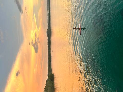       Person paddleboarding on calm water with a vibrant sunset in the background.
  