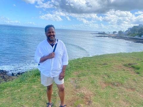 Smiling man standing on a grassy hill overlooking the ocean.