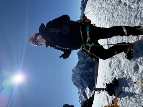 Man geared up for mountaineering standing on snow under a bright sun.