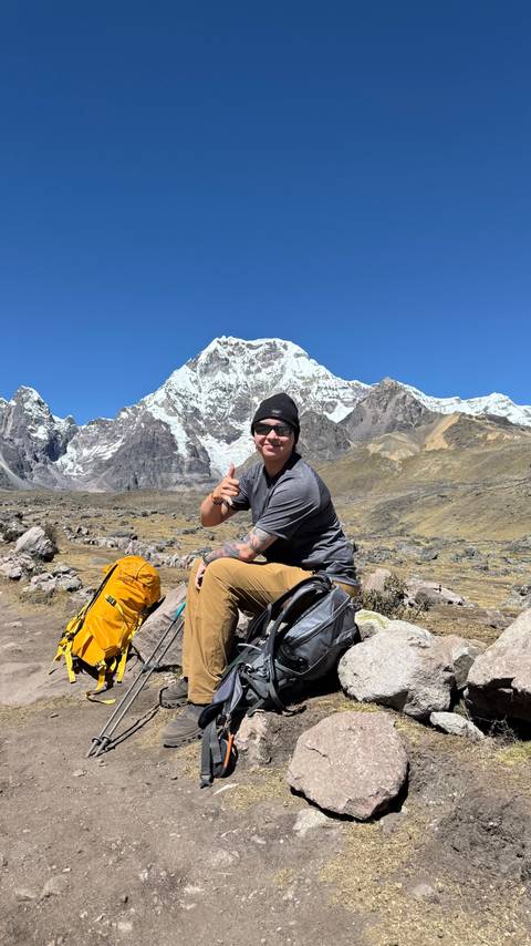 Man posing with a thumbs up, in front of a snowy mountain.