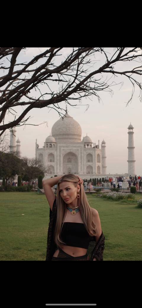 Woman posing in front of the Taj Mahal on a clear day.