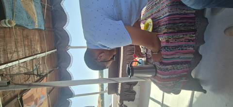       A person pouring a drink on a boat with a kettle and colorful textile.
  