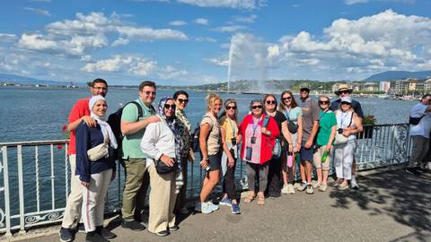      Group of tourists posing in front of a large fountain by a lake
  