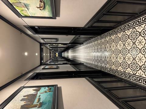       Long, ornate corridor with patterned tiles and paintings on the walls.
  