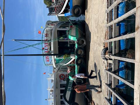       Docked boat with people walking nearby, set against a scenic backdrop.
  