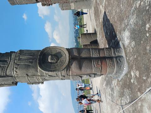       Tall ancient stone sculpture with tourists around.
  