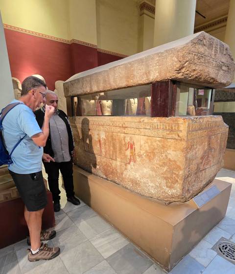 Indoor exhibit showing a sarcophagus with two people observing it.