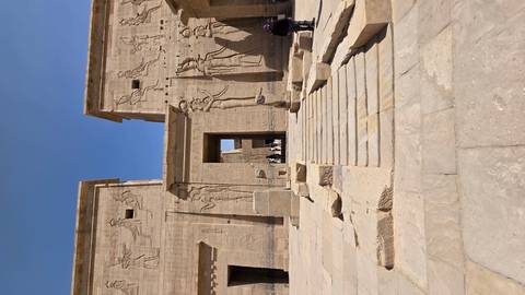       Temple entrance with tourists and carvings visible.
  