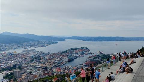       A panoramic view over a city and harbor with people observing.
  