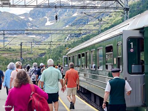       Tourists boarding the Flåm train surrounded by mountainous scenery.
  